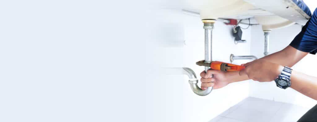 Close-up of a professional male plumber repairing white basin pipes with adjustable wrenches.